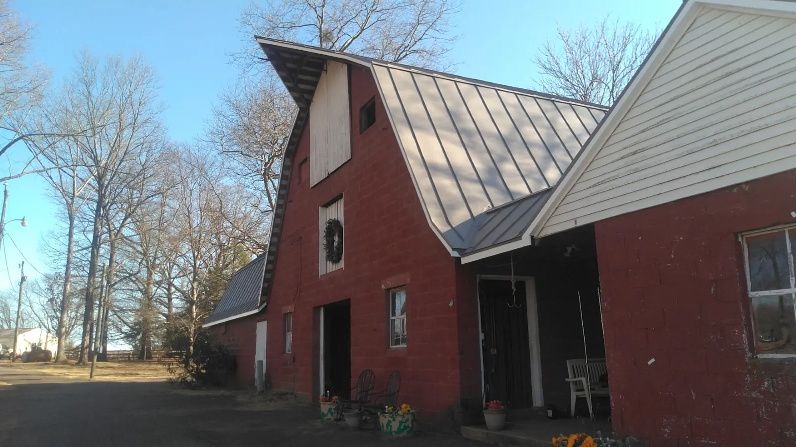 Red gambrel barn with a gray standing seam metal roof and a white-sided wing.