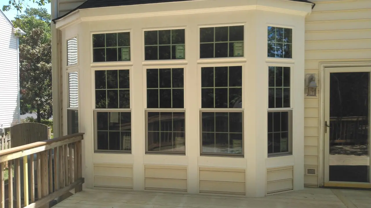 Wide bay of double-hung windows with white trim on a yellow-sided home above a wooden deck.