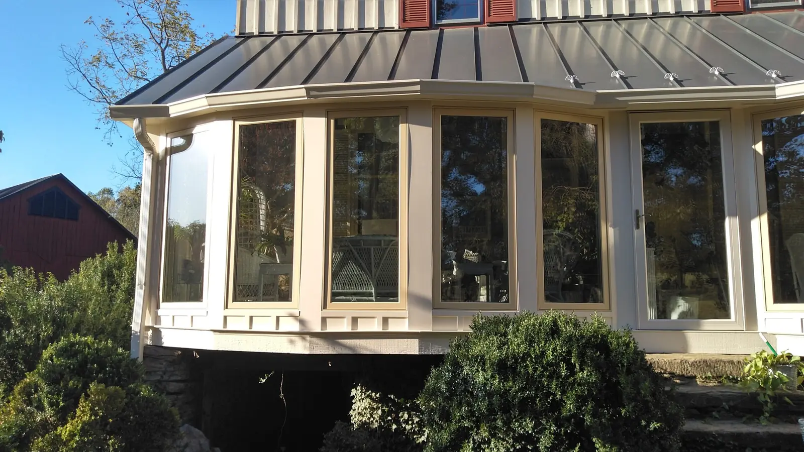 Bowed sunroom with cream-framed windows beneath a gray standing seam roof.