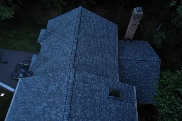 Aerial view of a blue-gray shingle roof with several planes and a brick chimney.