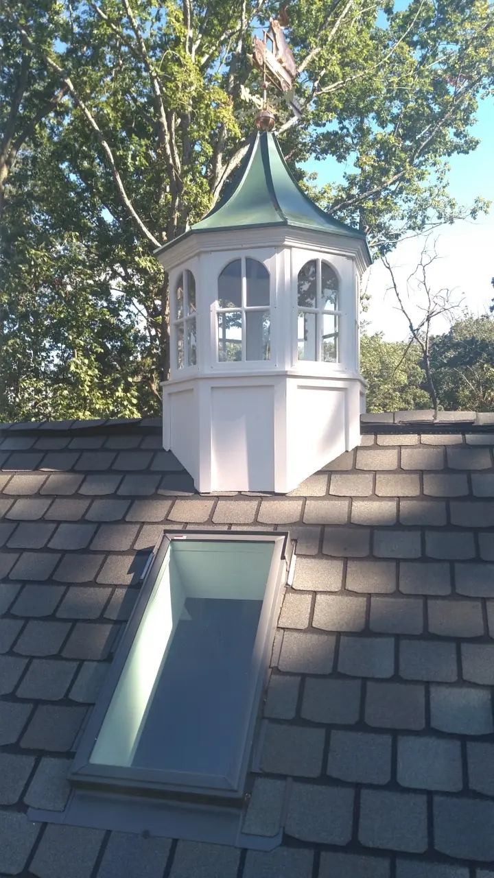 White cupola with a green cap and a skylight on slate-gray shingles.