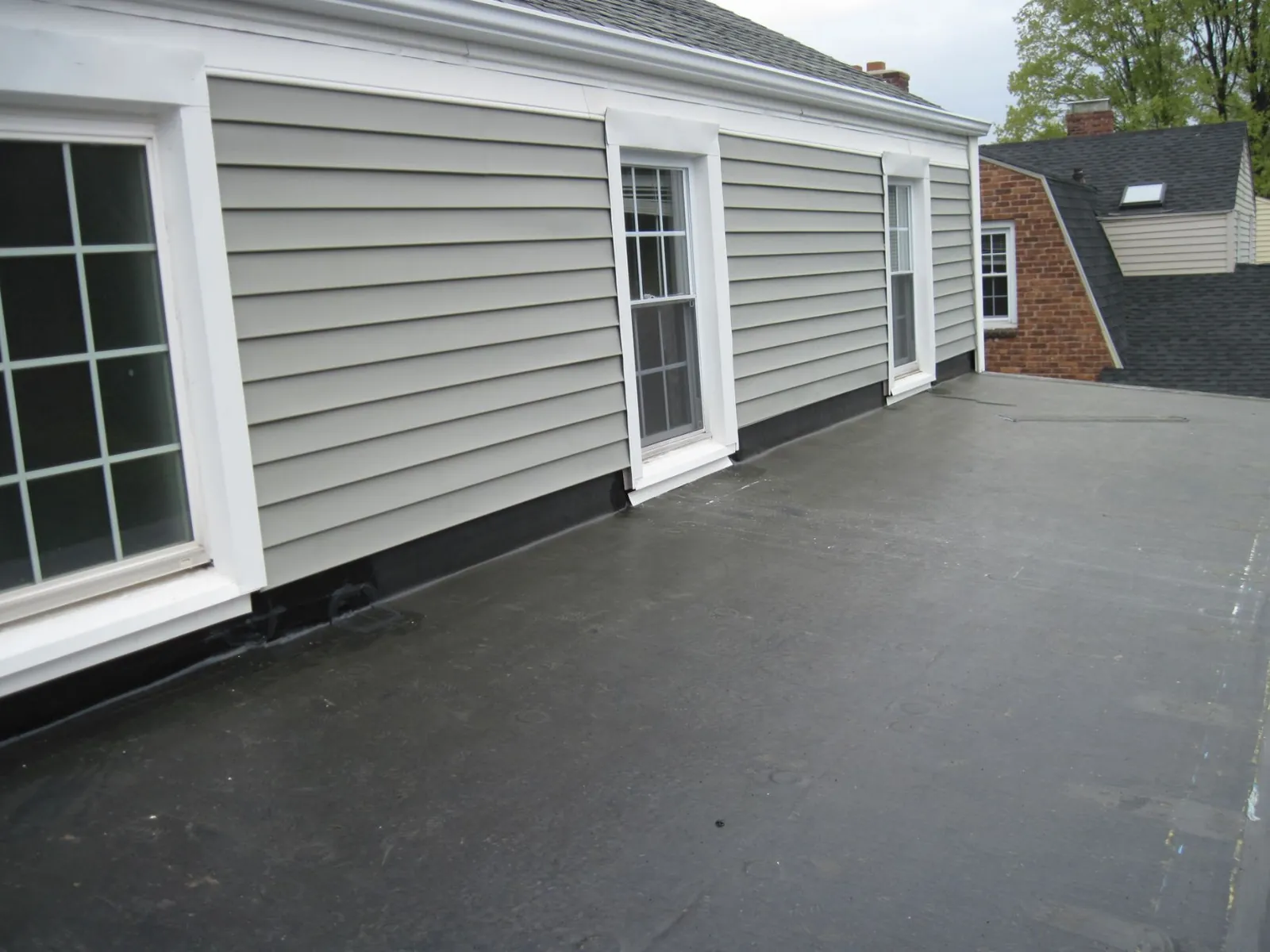 Black rubber flat roof membrane meeting grey siding and white-trimmed windows.