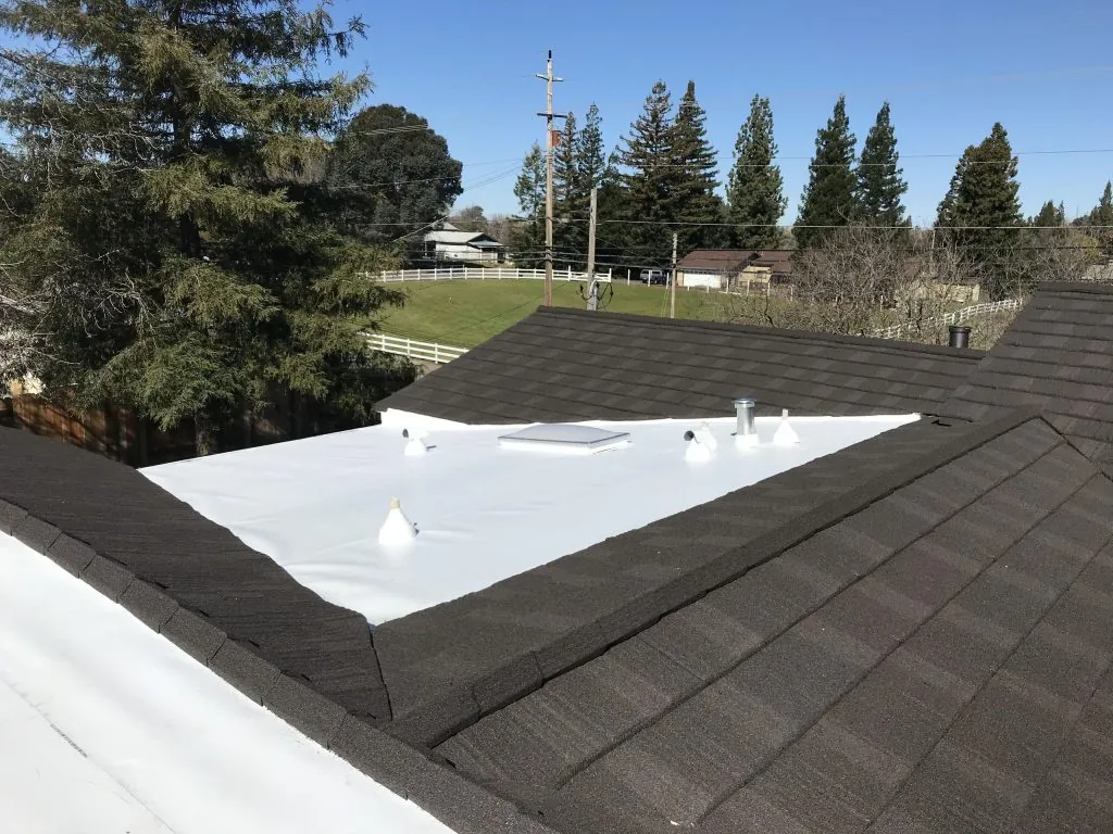 White flat roof membrane tied into a dark shingle roof with a vent penetration.