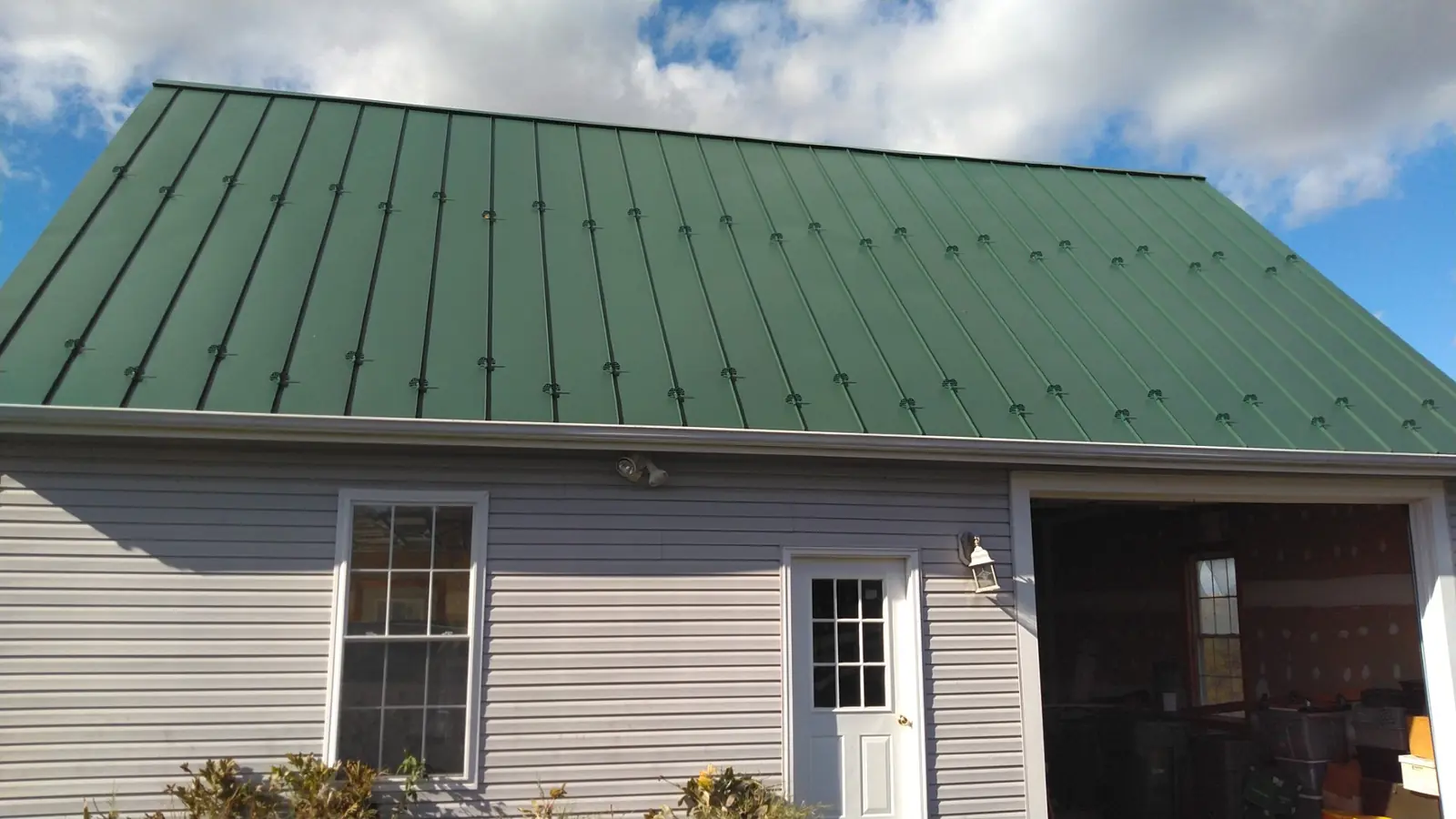 Garage roof before and after, side view: gray shingles then green standing seam