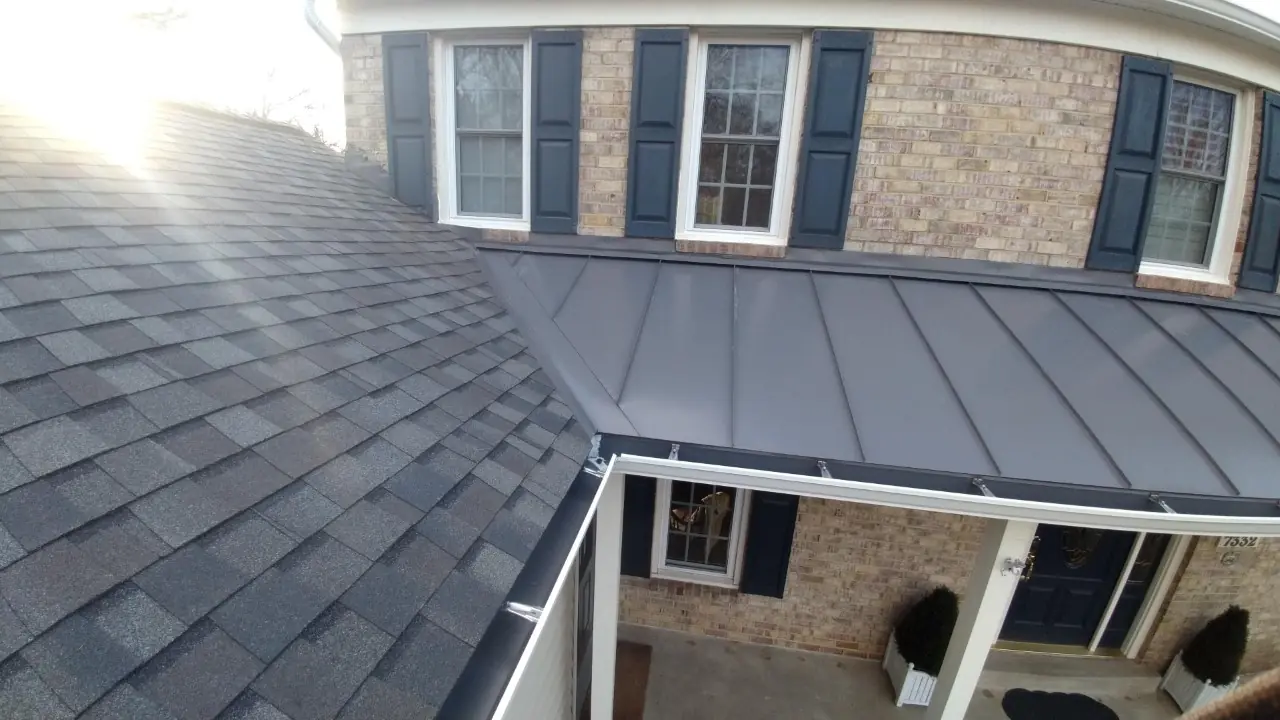 Gray standing seam porch roof beside dark shingles over a brick colonial with navy shutters.