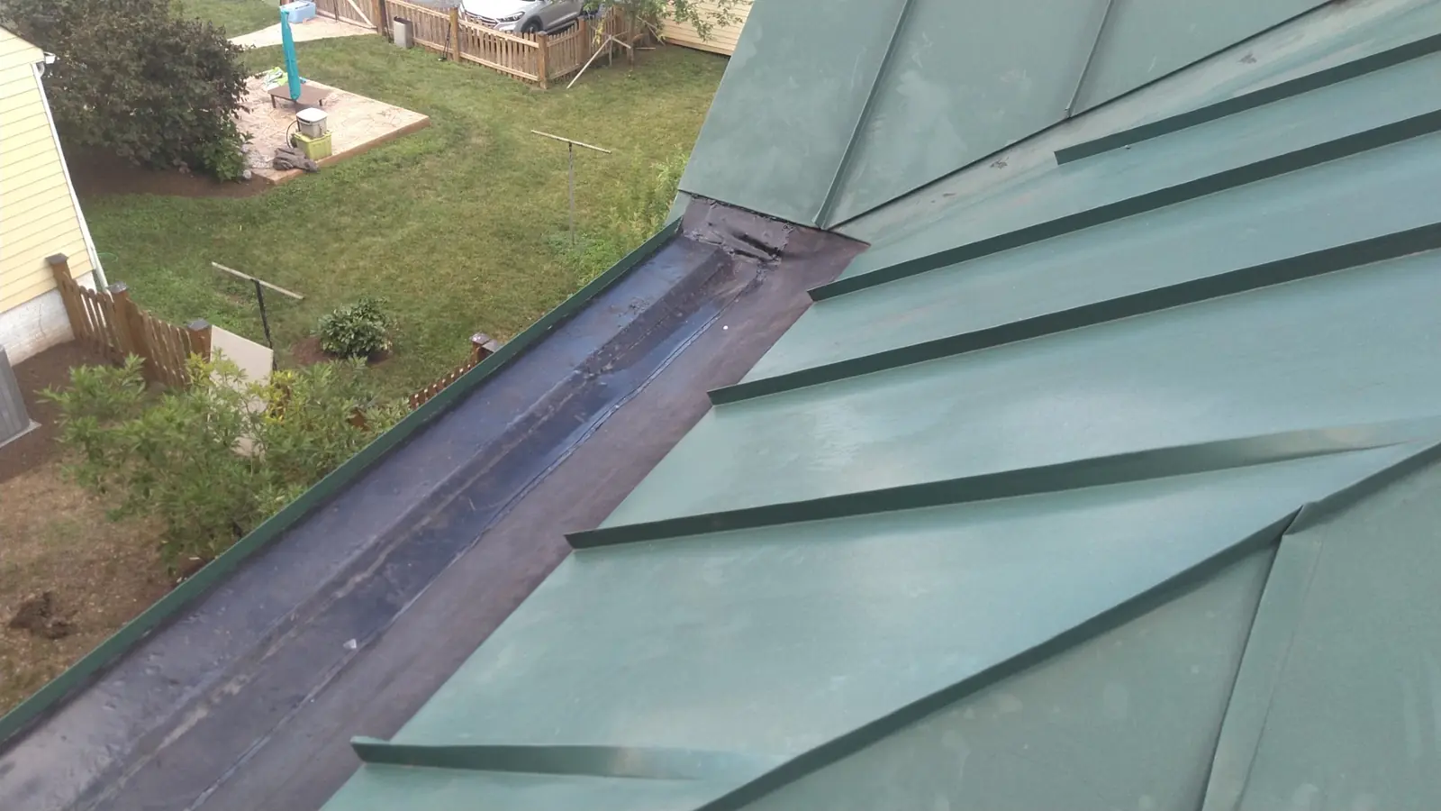 Box gutter lined with membrane beside green standing seam panels with raised seams.