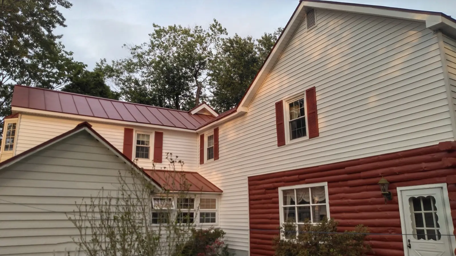 Two-story house with red standing seam roofs and a gable half covered in house wrap.