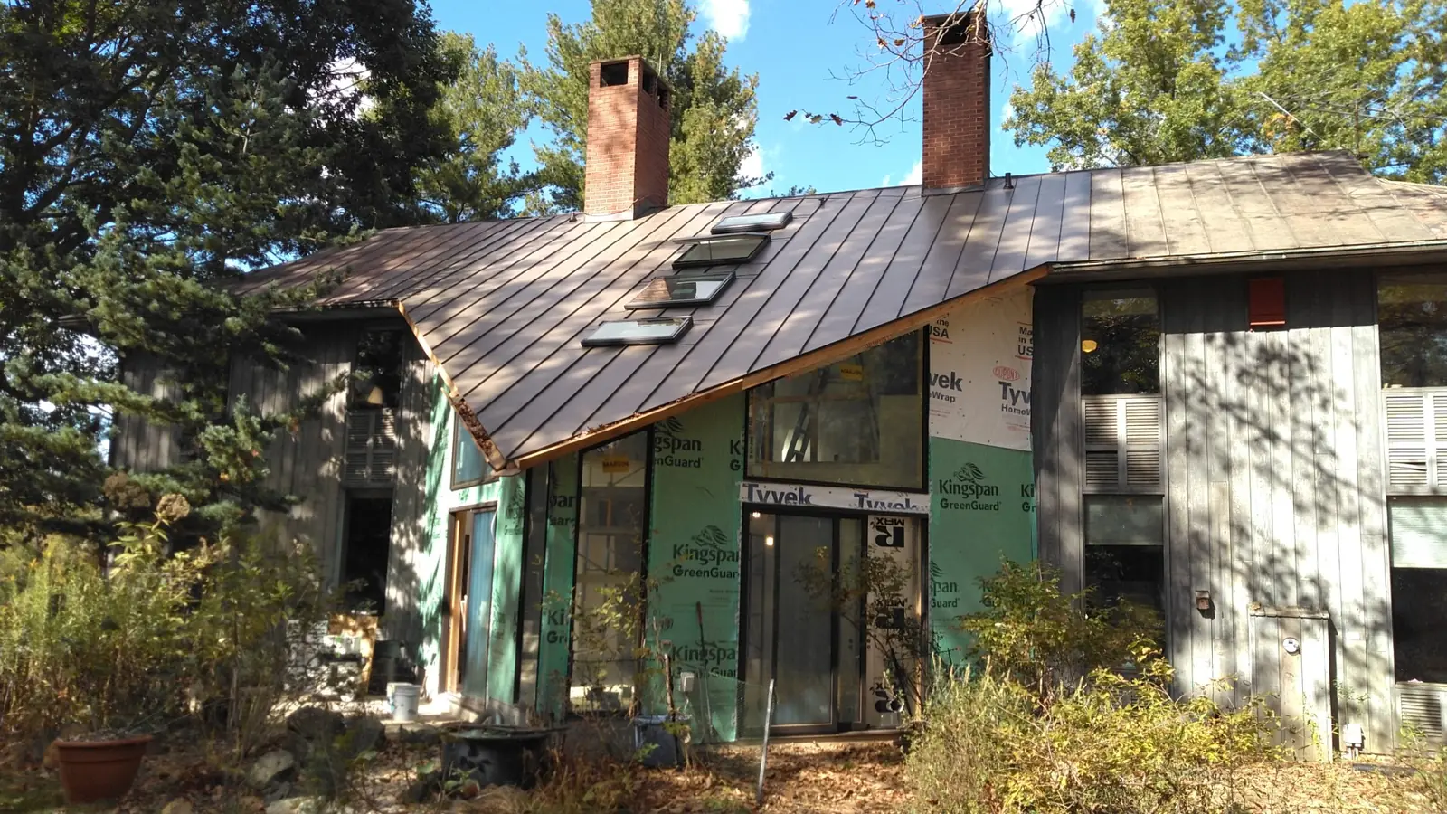 House under renovation with a bronze standing seam roof, skylights and two brick chimneys.