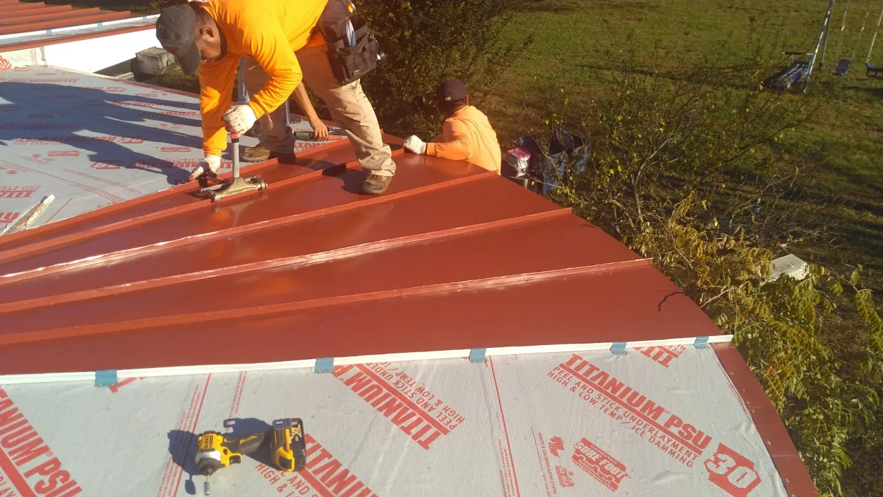 Stonewall crew members fastening red standing seam panels over synthetic underlayment.