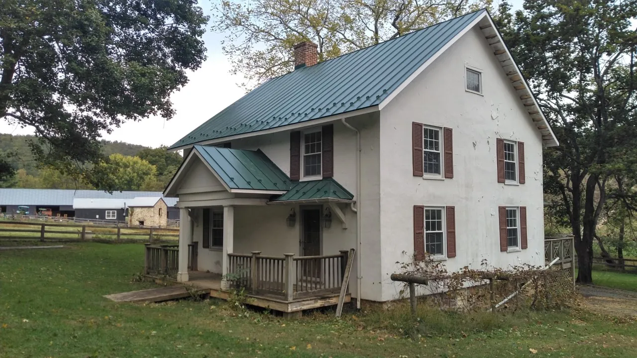 White farmhouse with a green standing seam metal roof and a covered porch.