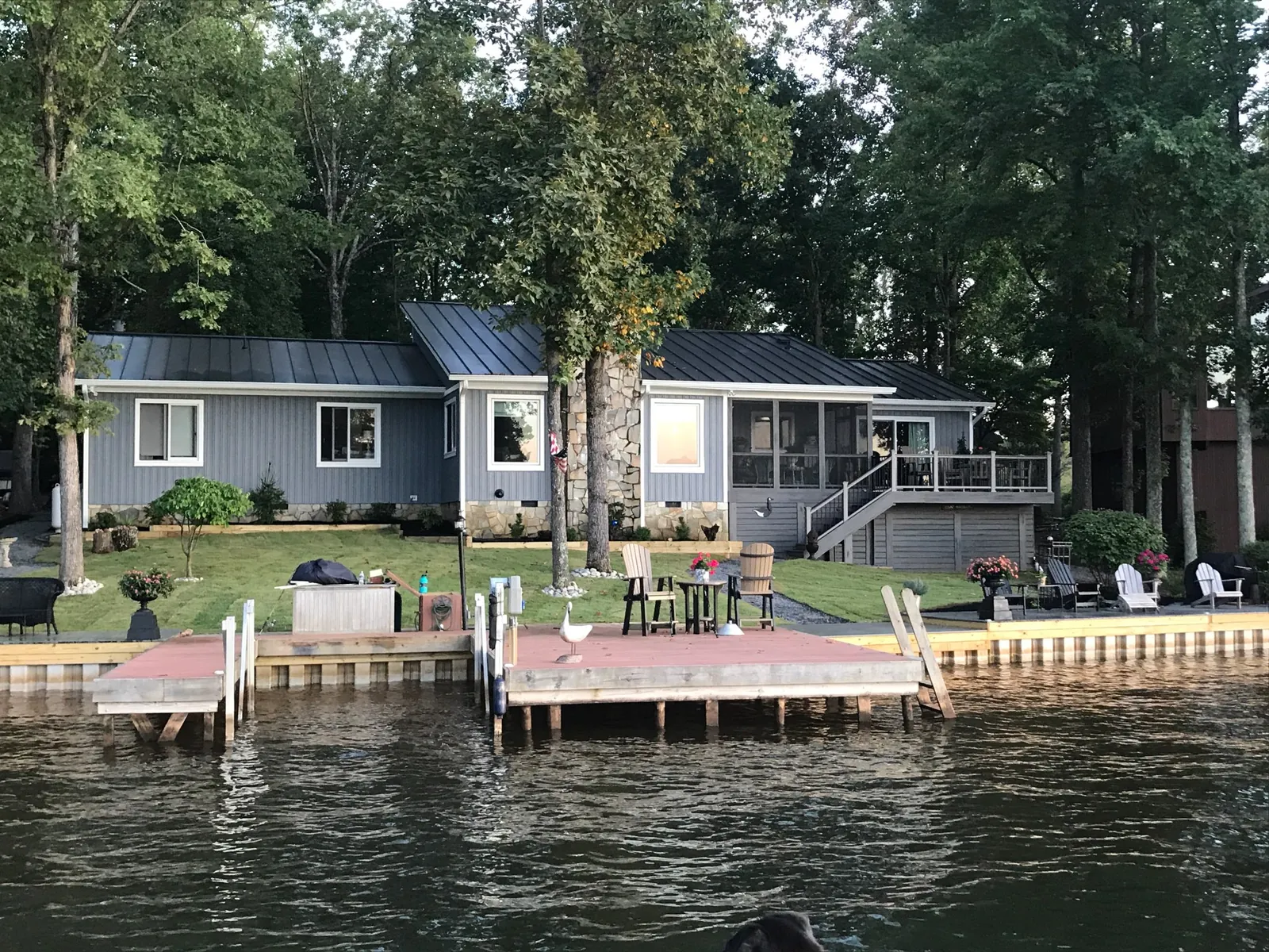 Lakeside ranch-style home with a dark metal roof, screened porch and a dock.