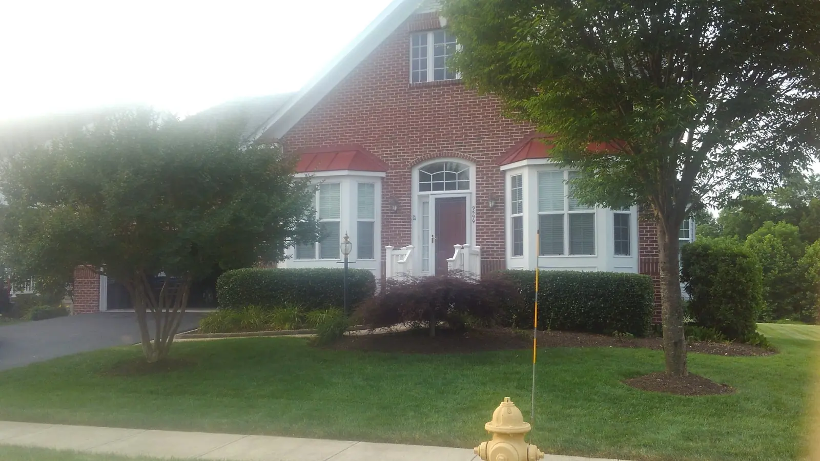 Brick home with red metal roofs over bay windows and a central entry.
