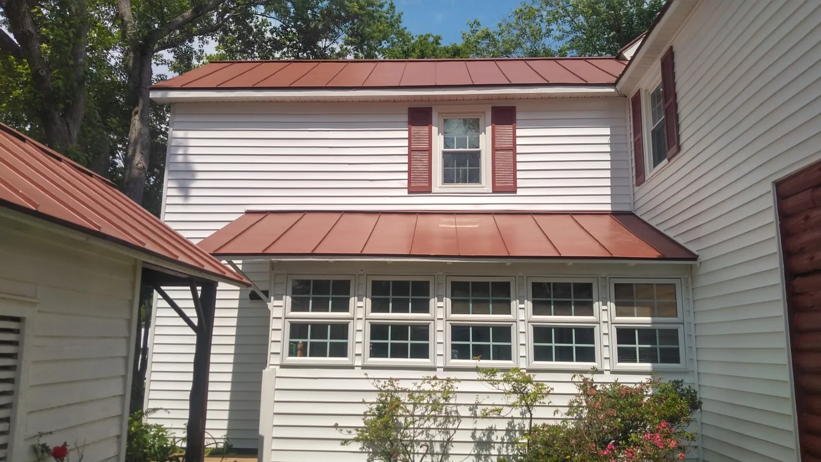 White home with red standing seam roofs over a porch and a bank of casement windows.