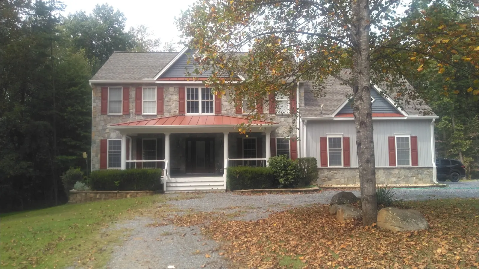 Front of a two-story home with gray siding, stone base and a red standing seam metal roof over the covered porch.
