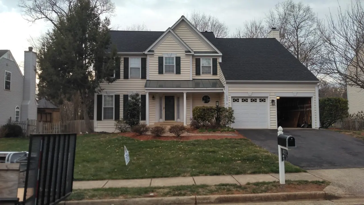 Two-story beige home with a dark roof, garage and a mailbox on a suburban street.