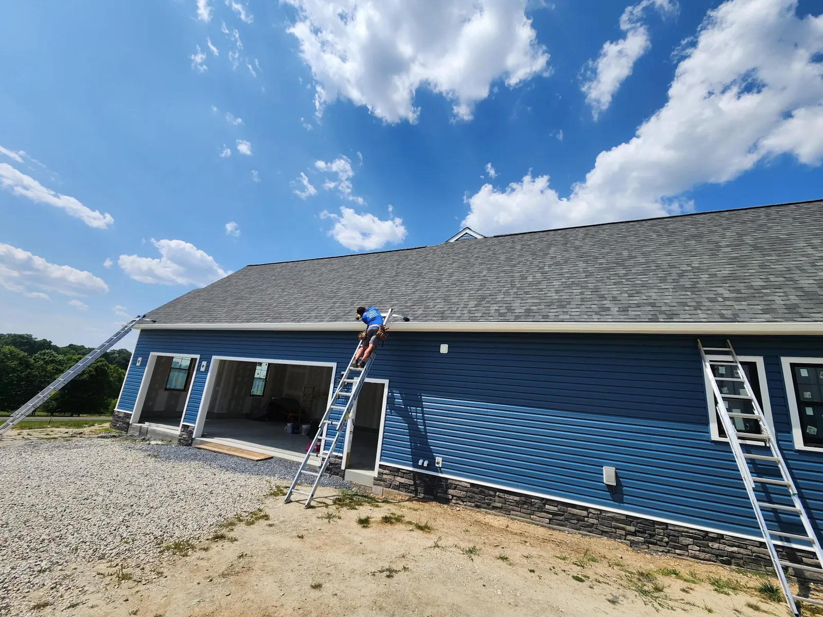 Long blue vinyl-sided home with fresh grey shingles and a ladder against the eave.