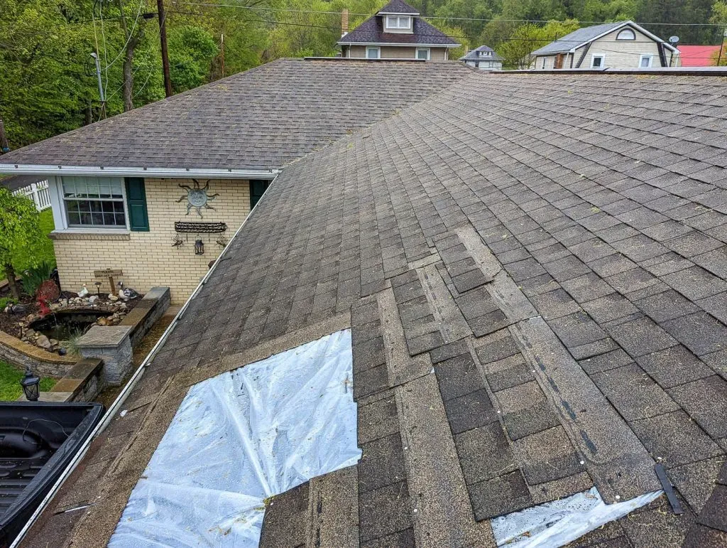 Roof with a section of shingles removed and protective sheeting laid for a repair.