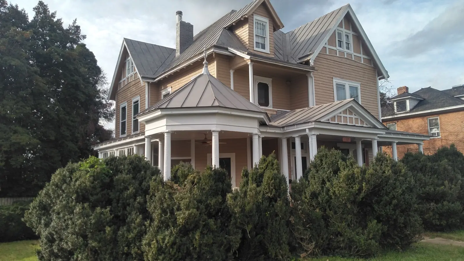 Tan Victorian-style home with a wraparound porch and slate gray standing seam roofs.