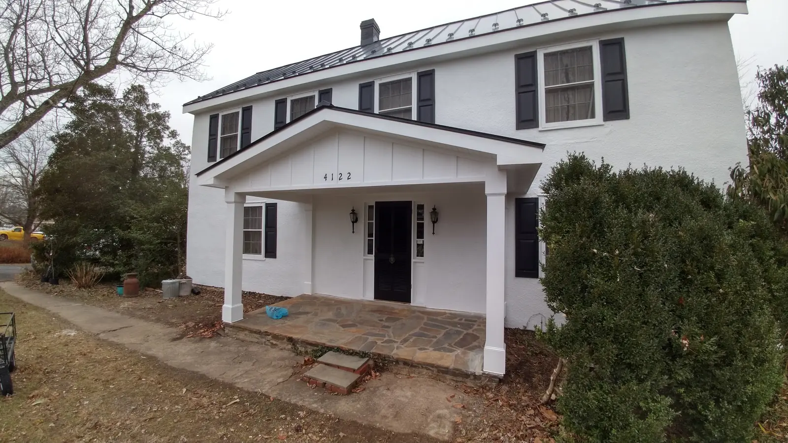 White colonial with a dark standing seam roof, a front porch and black shutters.
